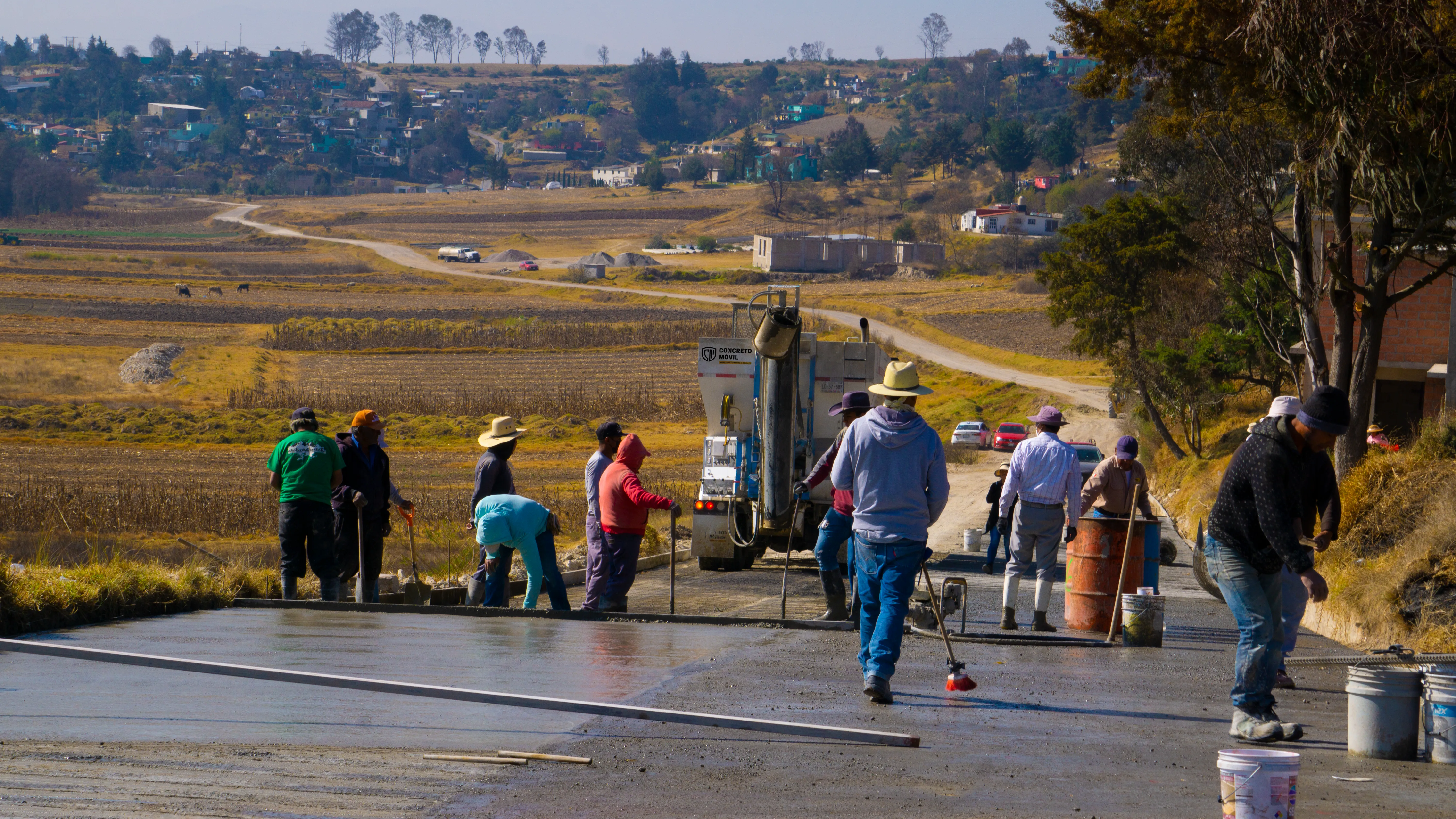 Trabajadores aplicando mezcla gris en calle, ideal para aprender Cómo Reducir Costos de Concreto en una Obra.